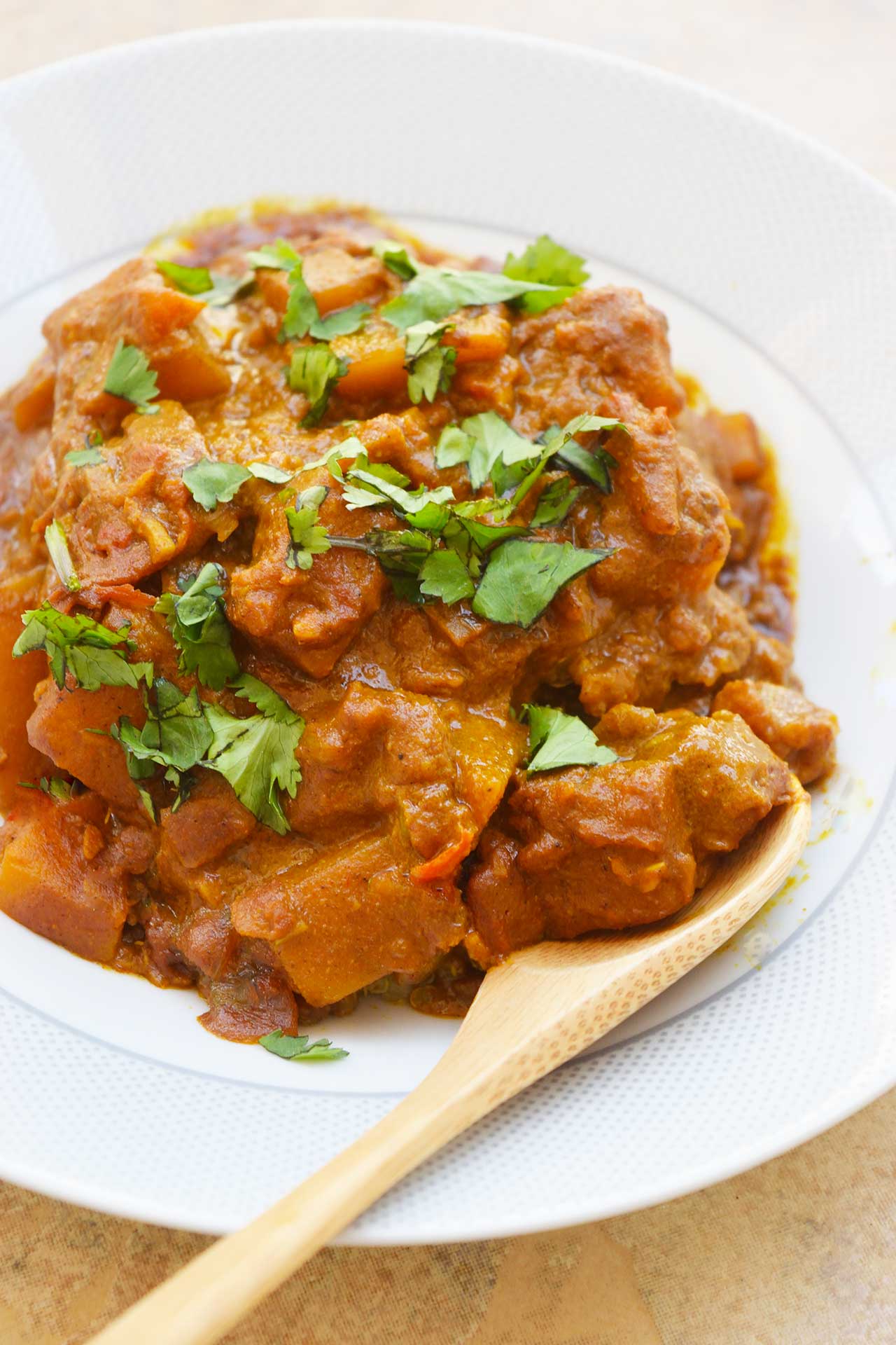 A closeup of a bowl full of Butternut Squash Curry with a wood spoon resting on the side of the bowl.