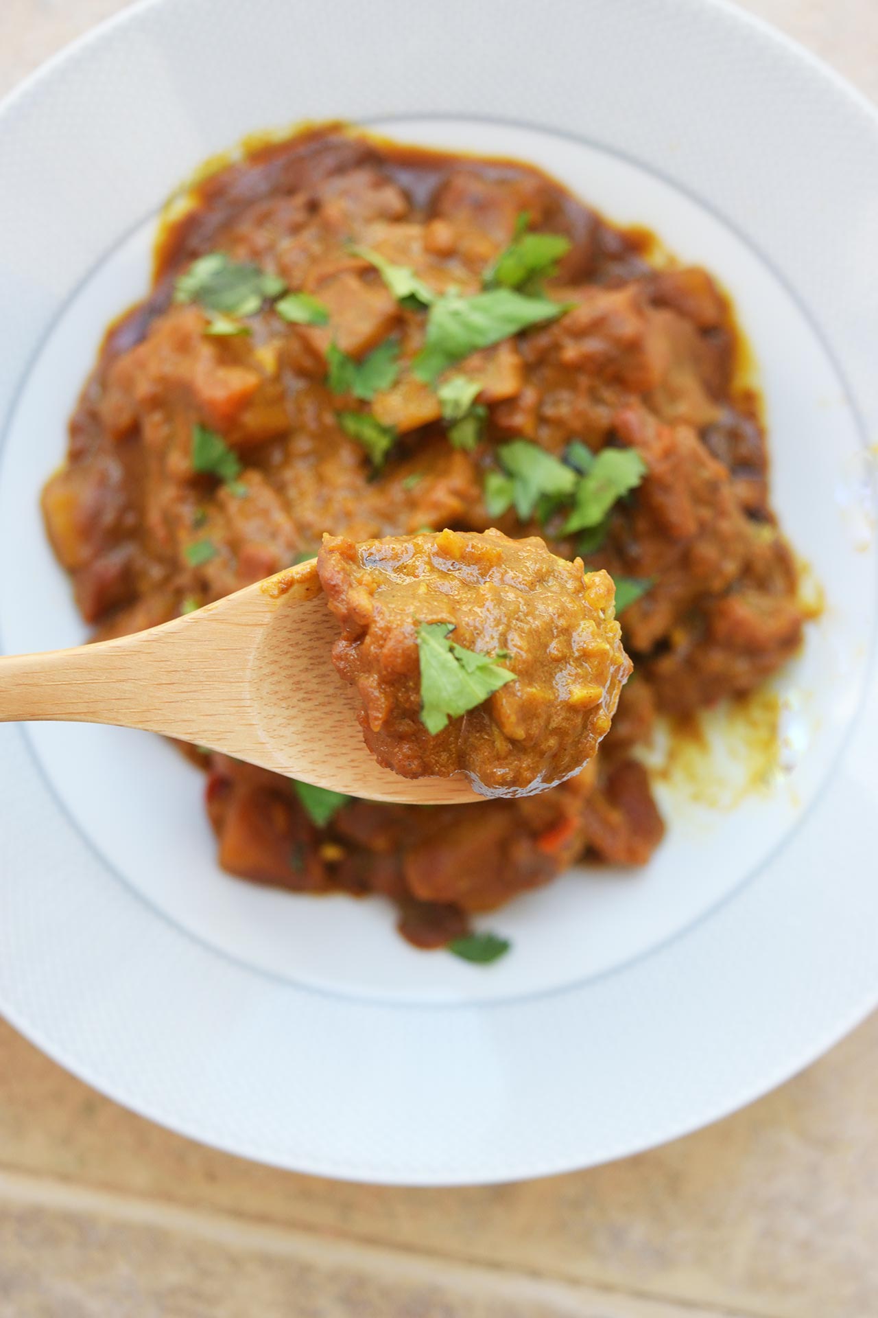 A wood spoon lifts a bite of Butternut Squash Curry from a bowl.