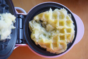 A cooked potato smashed on a waffle iron.