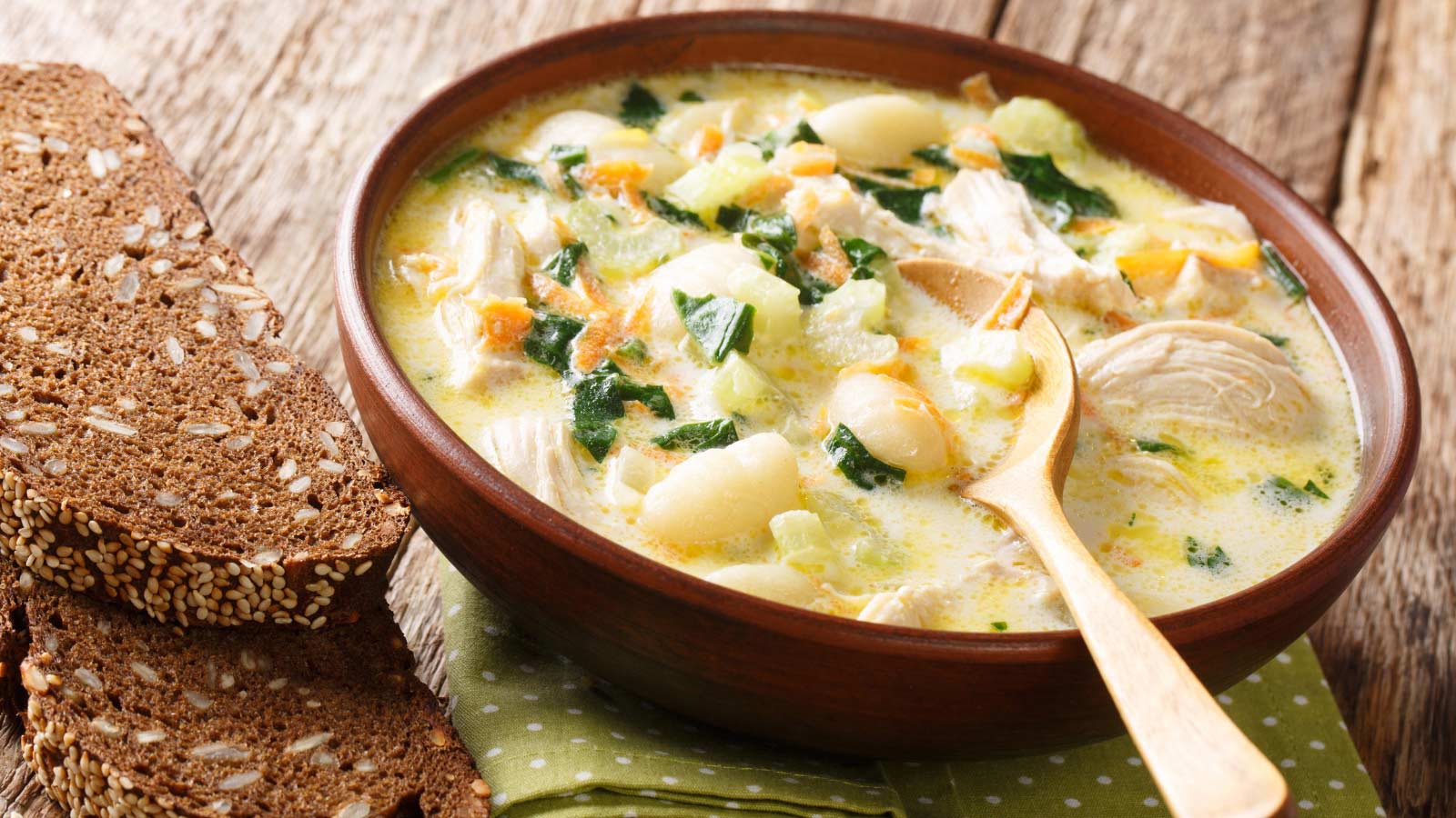 Homemade chicken and dumplings served with bread close-up in a bowl on a wood table.