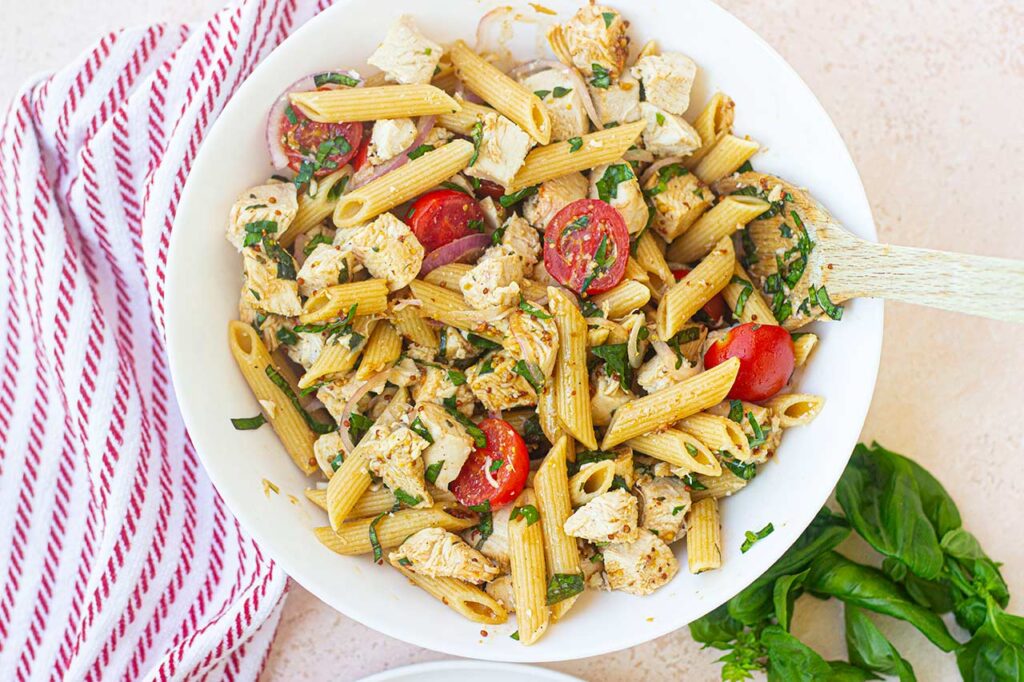Overhead view of a white bowl filled with chicken pasta salad.