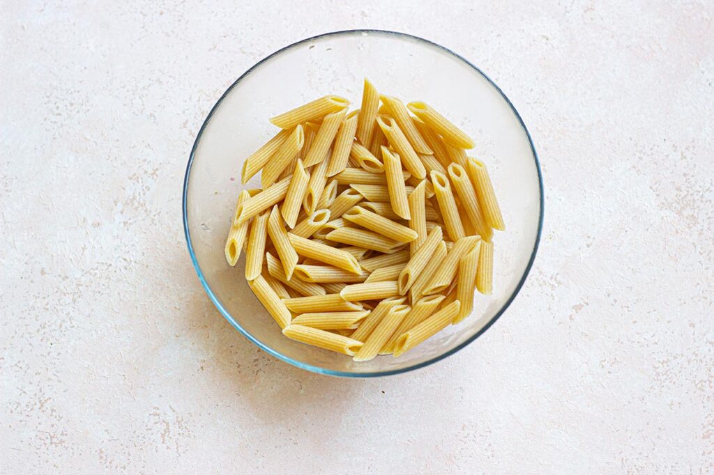 Cooked penne pasta in a glass mixing bowl.