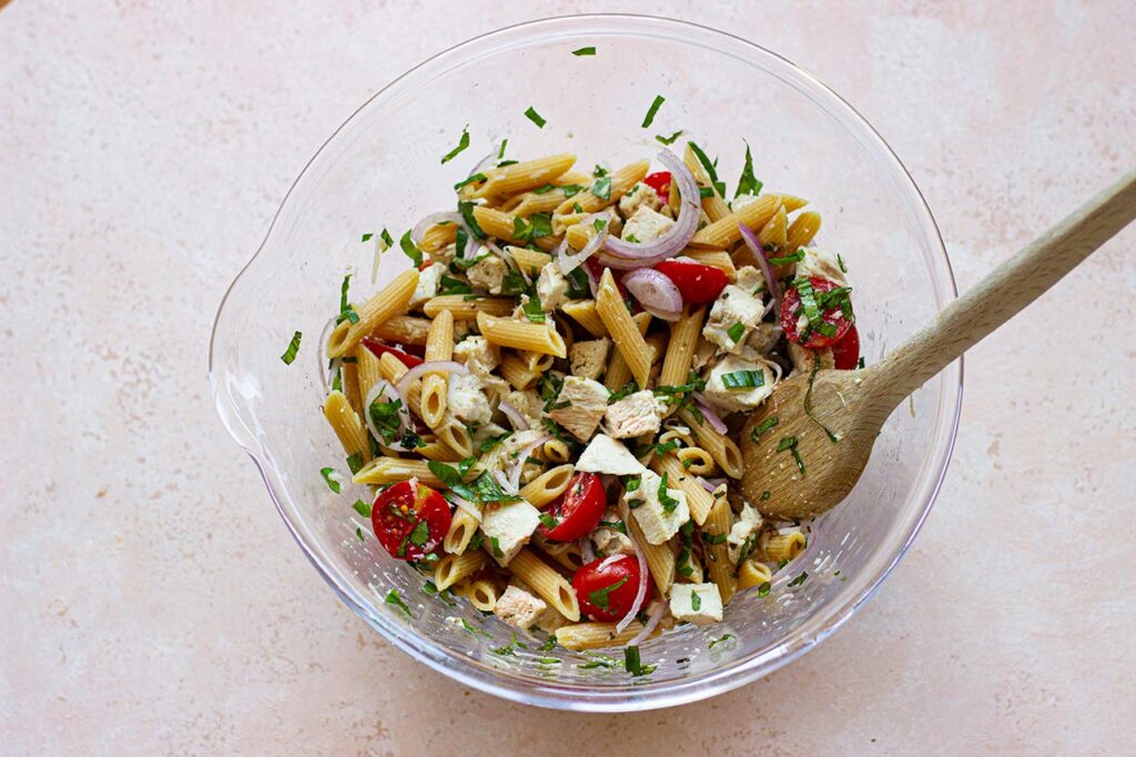 Tossing chicken pasta salad in a glass mixing bowl.