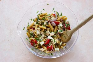 Tossing chicken pasta salad in a glass mixing bowl.
