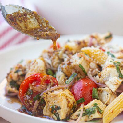 A spoon drizzled dressing over chicken pasta salad on a white plate.