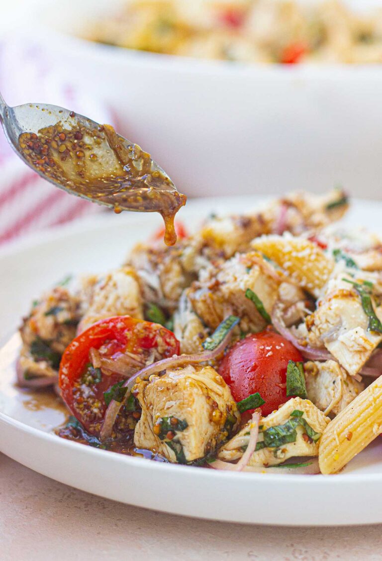 A spoon drizzled dressing over chicken pasta salad on a white plate.