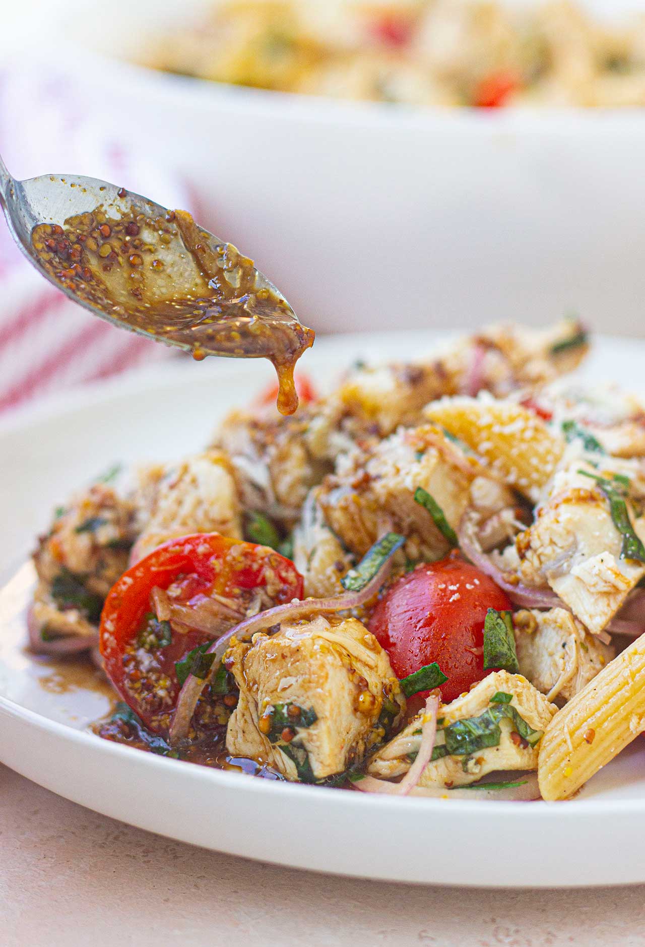 A spoon drizzled dressing over chicken pasta salad on a white plate.