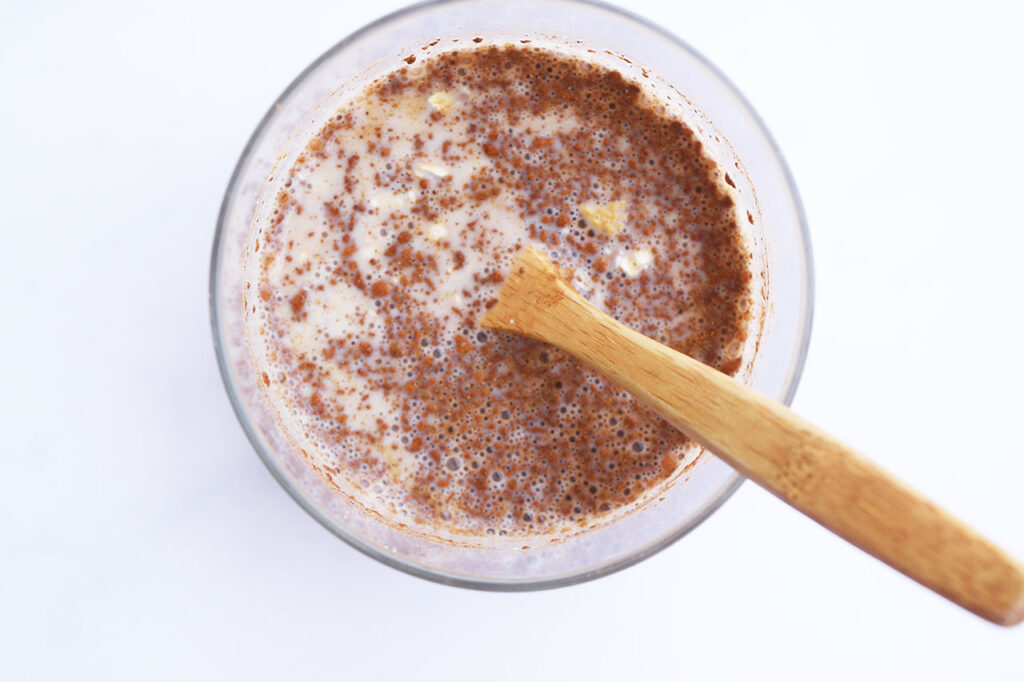 Cranberry Overnight Oats ingredients mixed together in a glass jar with a wooden spoon.