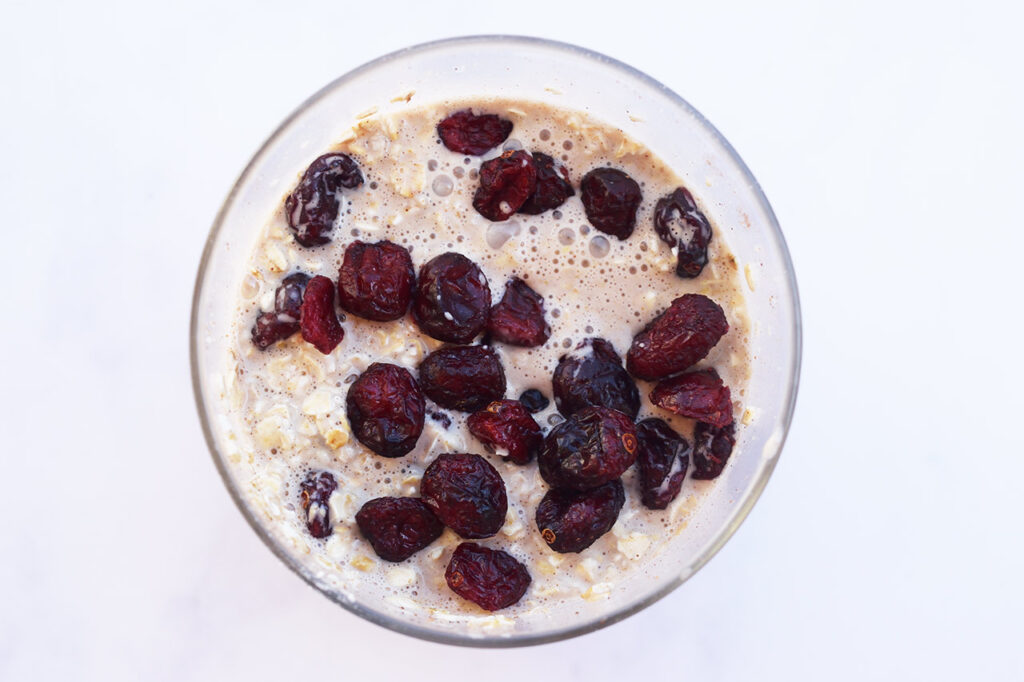 Dried cranberries added to soaked oats in a glass jar.