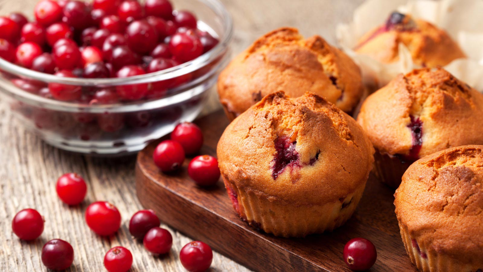 Muffins with cranberries, cranberries in a glass bowl on the old wooden background.