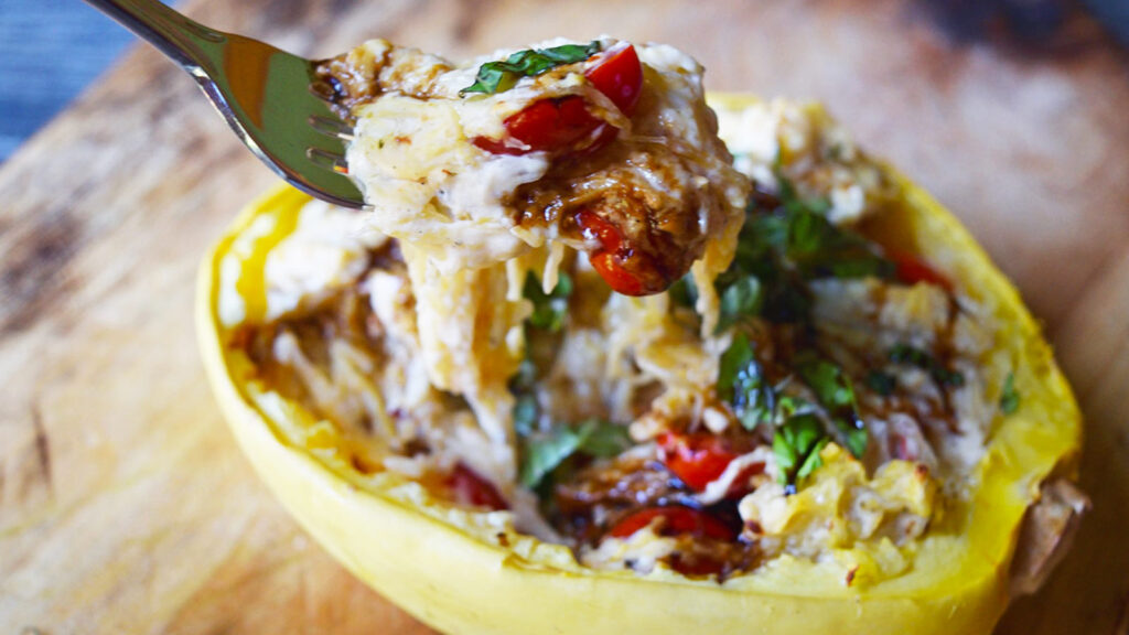 A fork lifts a forkful of creamy stuffed spaghetti squash from a squash half.