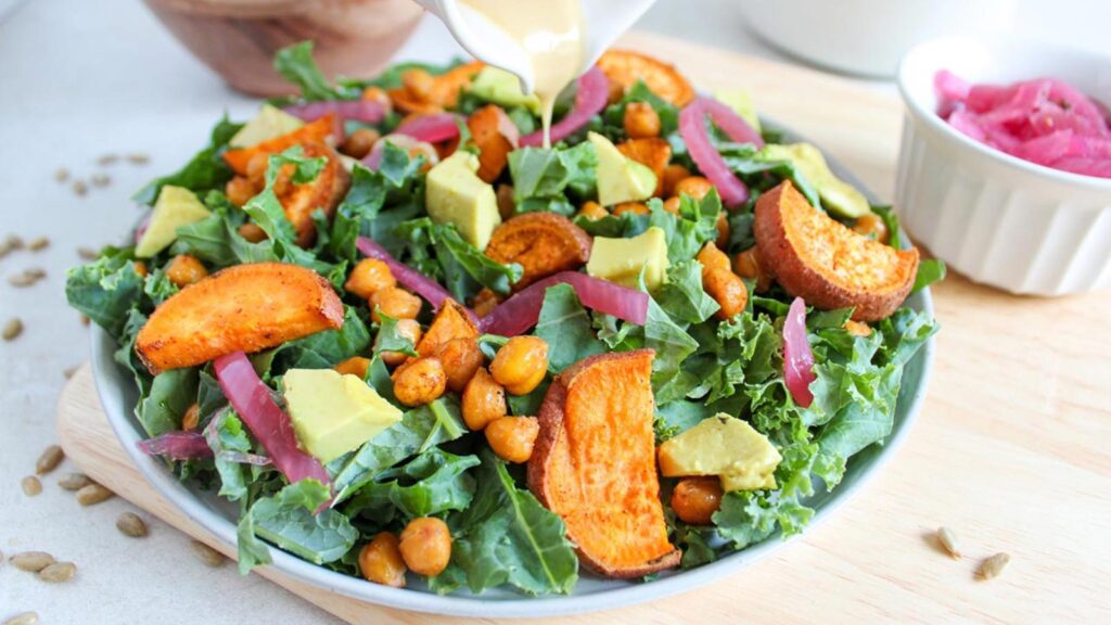 Dressing being poured over a fall harvest salad in na white bowl.