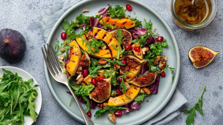 Grilled pumpkin, fig, pomegranate and walnut salad on blue plate, top view