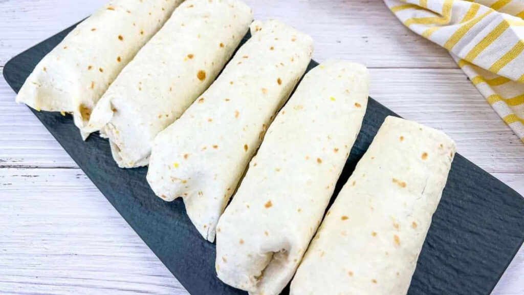A row of breakfast burritos on a slate board.