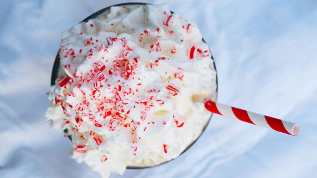 An overhead view of a Homemade Peppermint Mocha topped with whipped cream, crushed candy cane and a red and white striped straw.