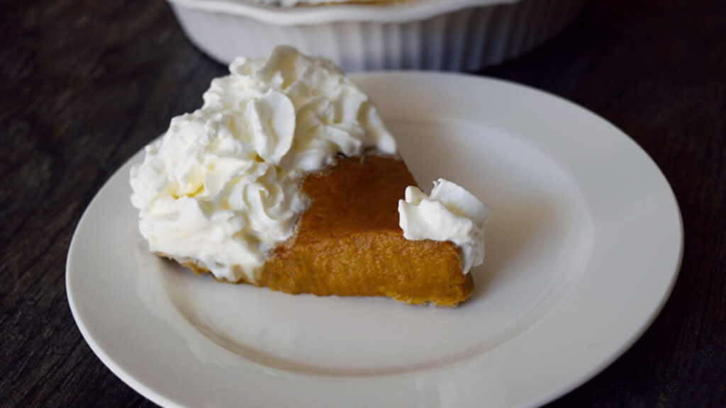 A single slice of Kabocha Pie served on a white plate and topped with whipped cream.