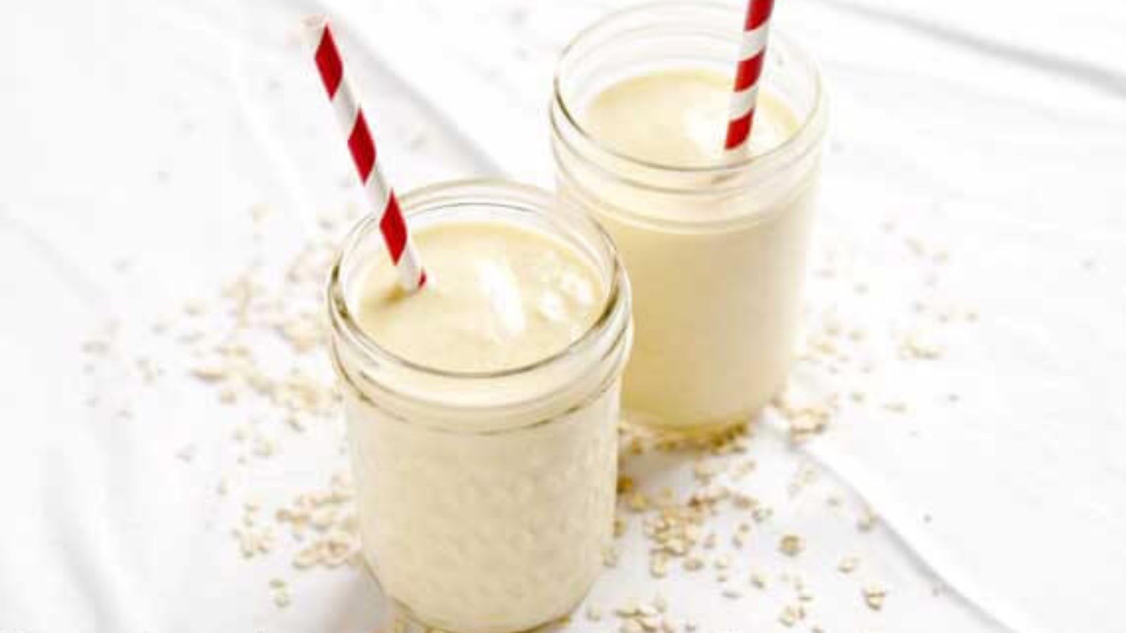 Two glass jars filled with Mango Oatmeal Smoothie. A red and white stripped straw in each glass.