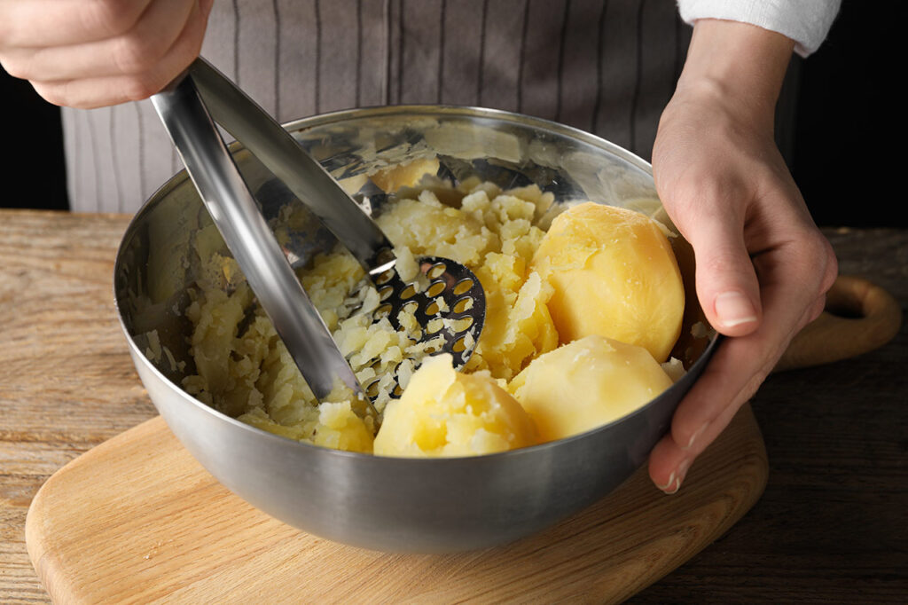 Woman making mashed potato at wooden table, closeup