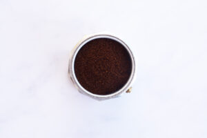 Moka pot coffee basket filled with coffee and sitting in the bottom section.