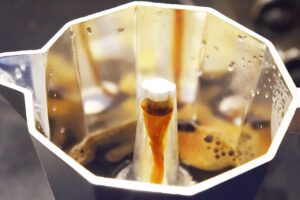 Coffee gently flowing over the nozzle in an open Moka pot.