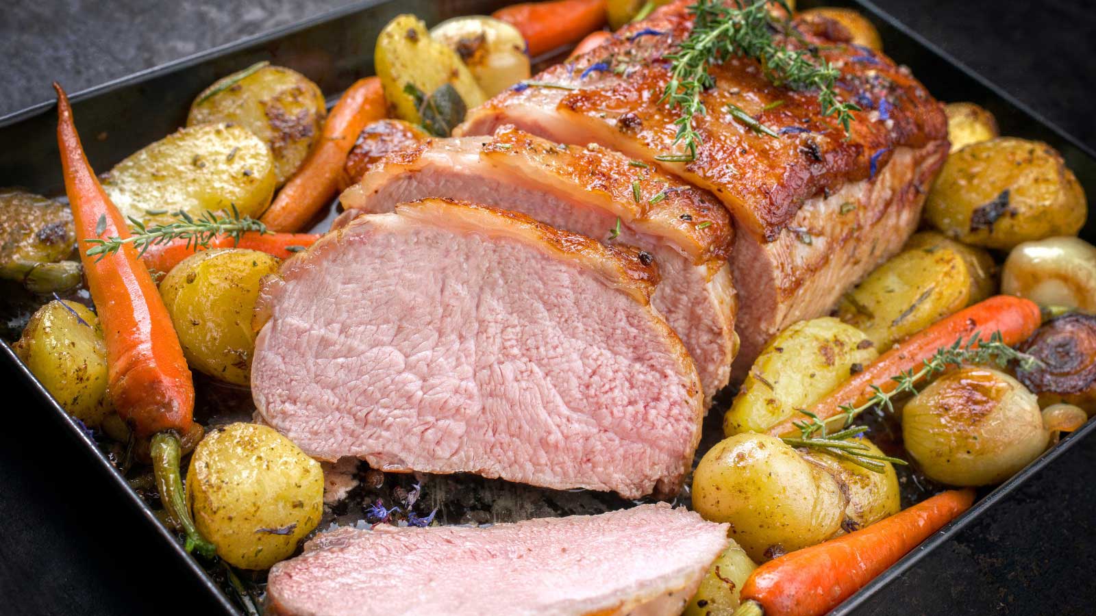 Traditional roasted dry aged veal tenderloin with carrots and potatoes offered as closeup on a metal tray.