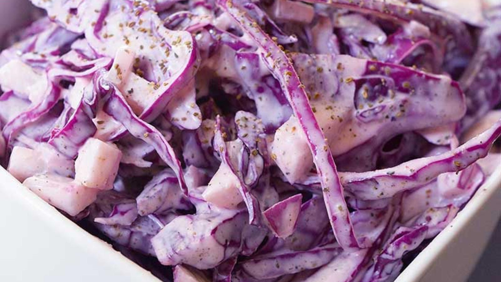 A closeup of a white bowl filled with red cabbage slaw.