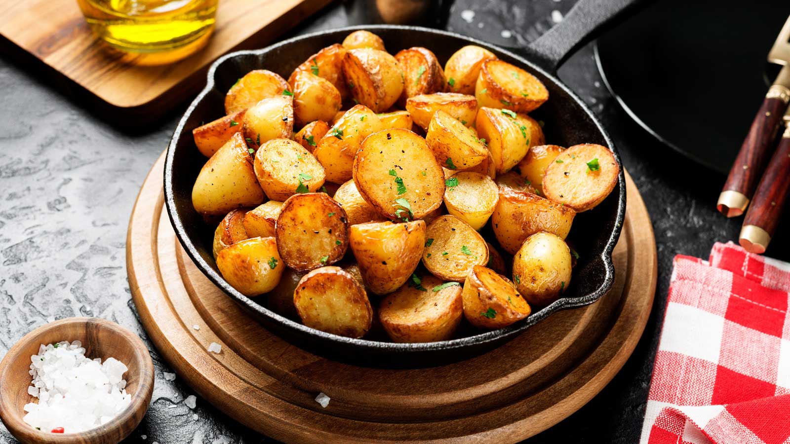 Roasted baby potatoes in iron skillet on black background.