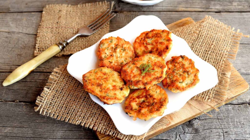Salmon patties on a plate and on cutting board. Fork on a burlap on an old wooden background.