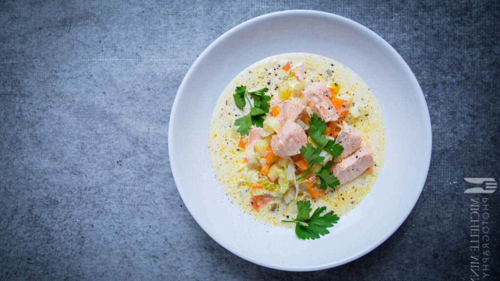 A white bowl filled partway with salmon soup. Gray background.