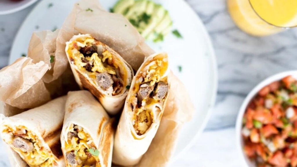 Two sausage breakfast burritos cut in half and placed in a holder with parchment.
