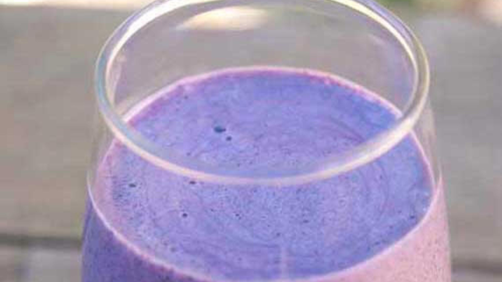 A closeup of a clear glass with a purple smoothie in it.