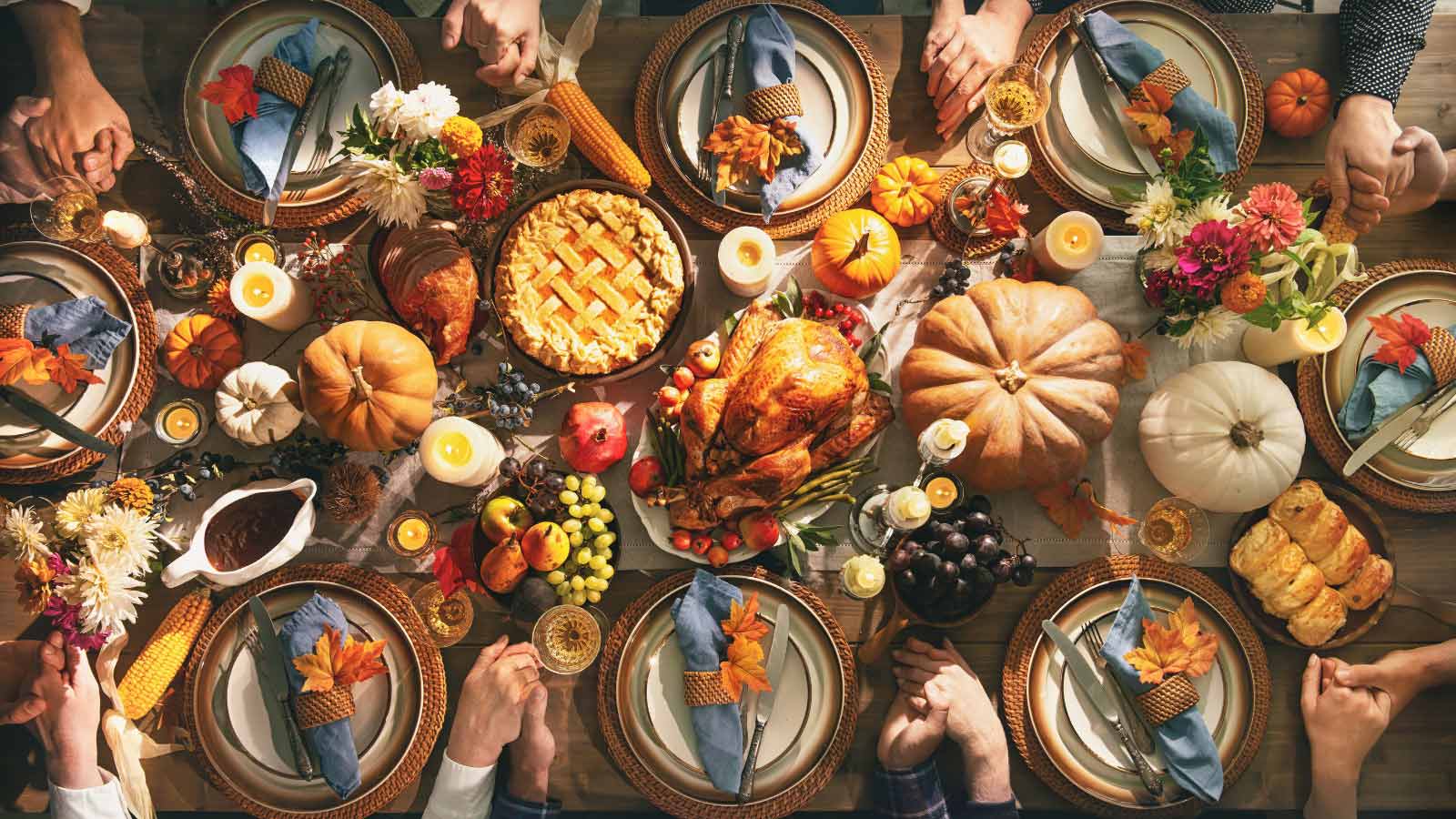 Group of friends or family members giving thanks to God at festive turkey dinner table together. Thanksgiving celebration traditional dinner concept.