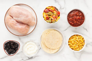 Slow Cooker Tortilla Chicken Stew ingredients in individual bowls on a white, marble surface.
