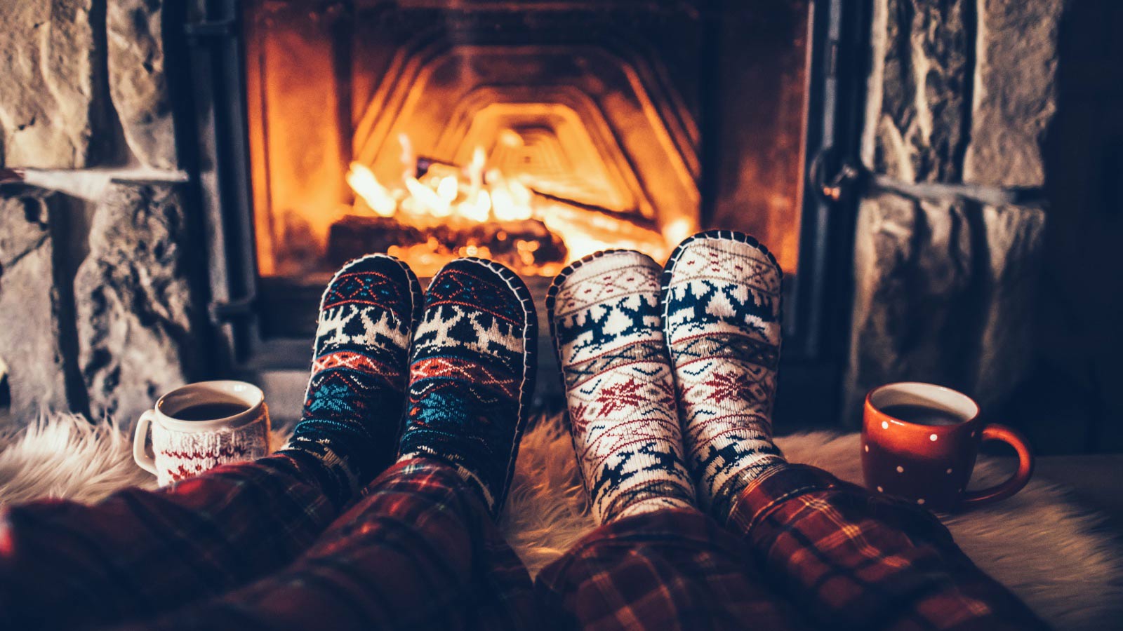 Feet in woollen socks by the Christmas fireplace. Couple sitting under the blanket, relaxes by warm fire and warming up their feet in woollen socks. Winter and Christmas holidays concept.