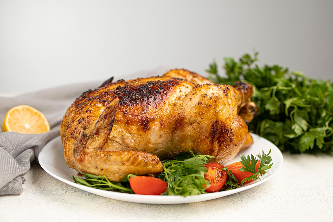 Side view of a Whole Roasted Chicken on a white platter.