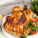 Partial overhead view of a Whole Roasted Chicken on a white platter.