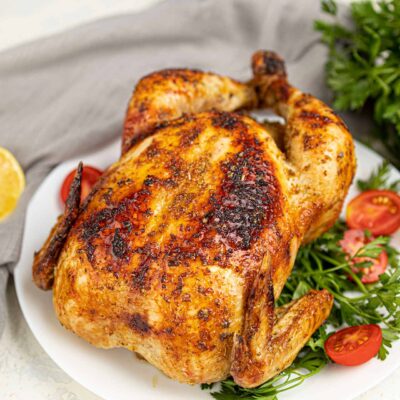 Partial overhead view of a Whole Roasted Chicken on a white platter.