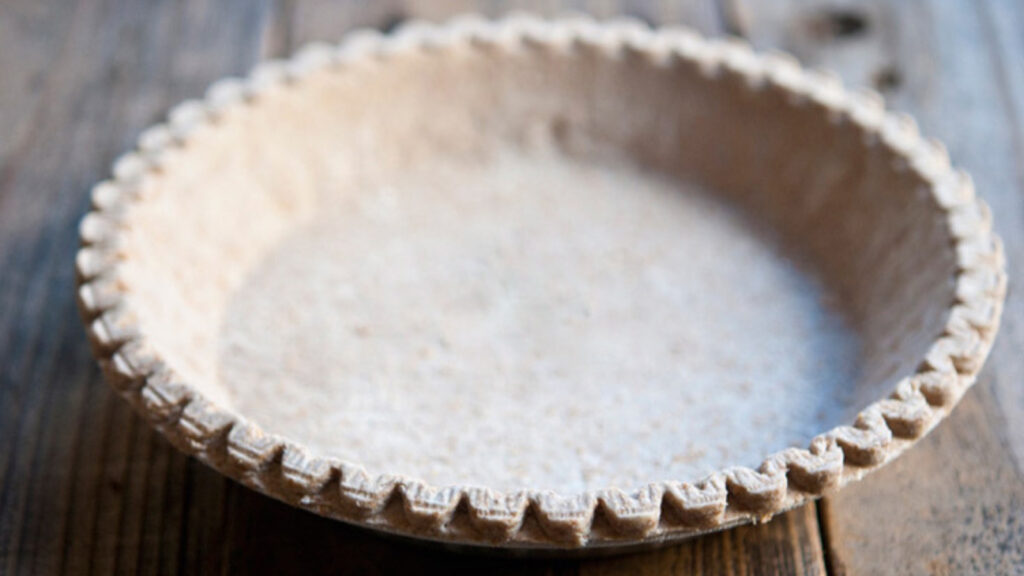 A whole wheat pie crust with a stamped edge on a wood surface.