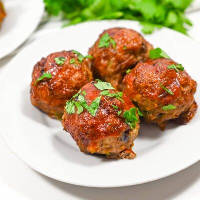 Four Air Fryer Meatballs on a white plate with fresh parsley sprinkled over the top.