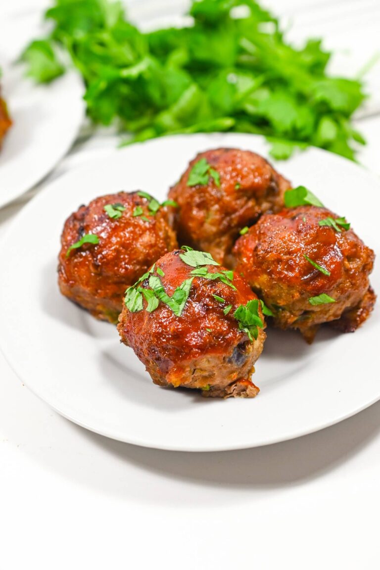 Four Air Fryer Meatballs on a white plate with fresh parsley sprinkled over the top.