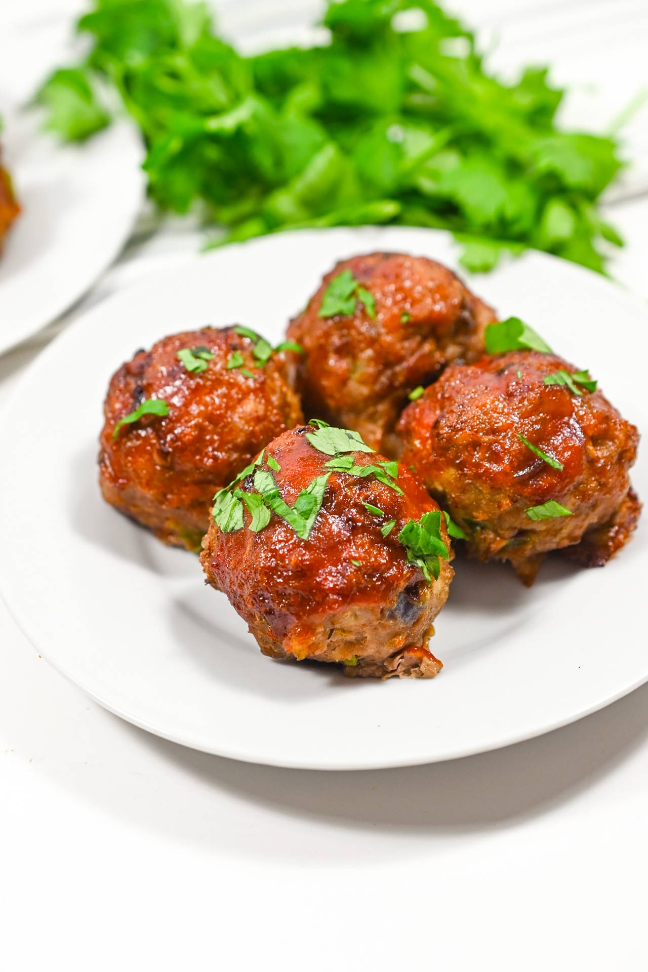 Four Air Fryer Meatballs on a white plate with fresh parsley sprinkled over the top.