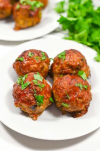 Front view of four Air Fryer Meatballs on a white plate with fresh parsley sprinkled over the top.