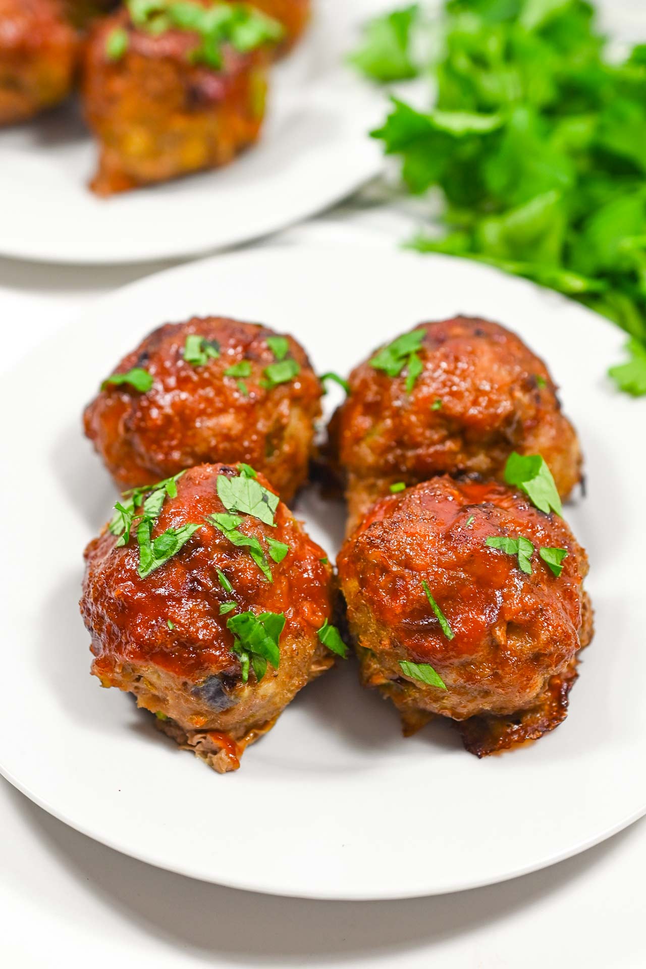 Front view of four Air Fryer Meatballs on a white plate with fresh parsley sprinkled over the top.