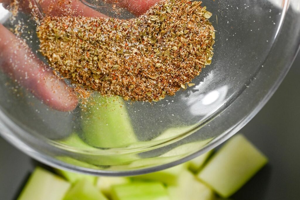 Sprinkling spice mix over cut zucchini pieces.