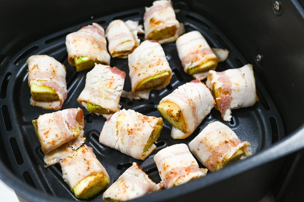 Uncooked Bacon-Wrapped Zucchini bites in an air fryer basket.