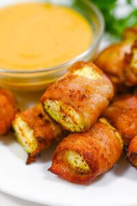 Closeup of a pile of Bacon-Wrapped Zucchini on a white plate.