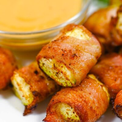 Closeup of a pile of Bacon-Wrapped Zucchini on a white plate.