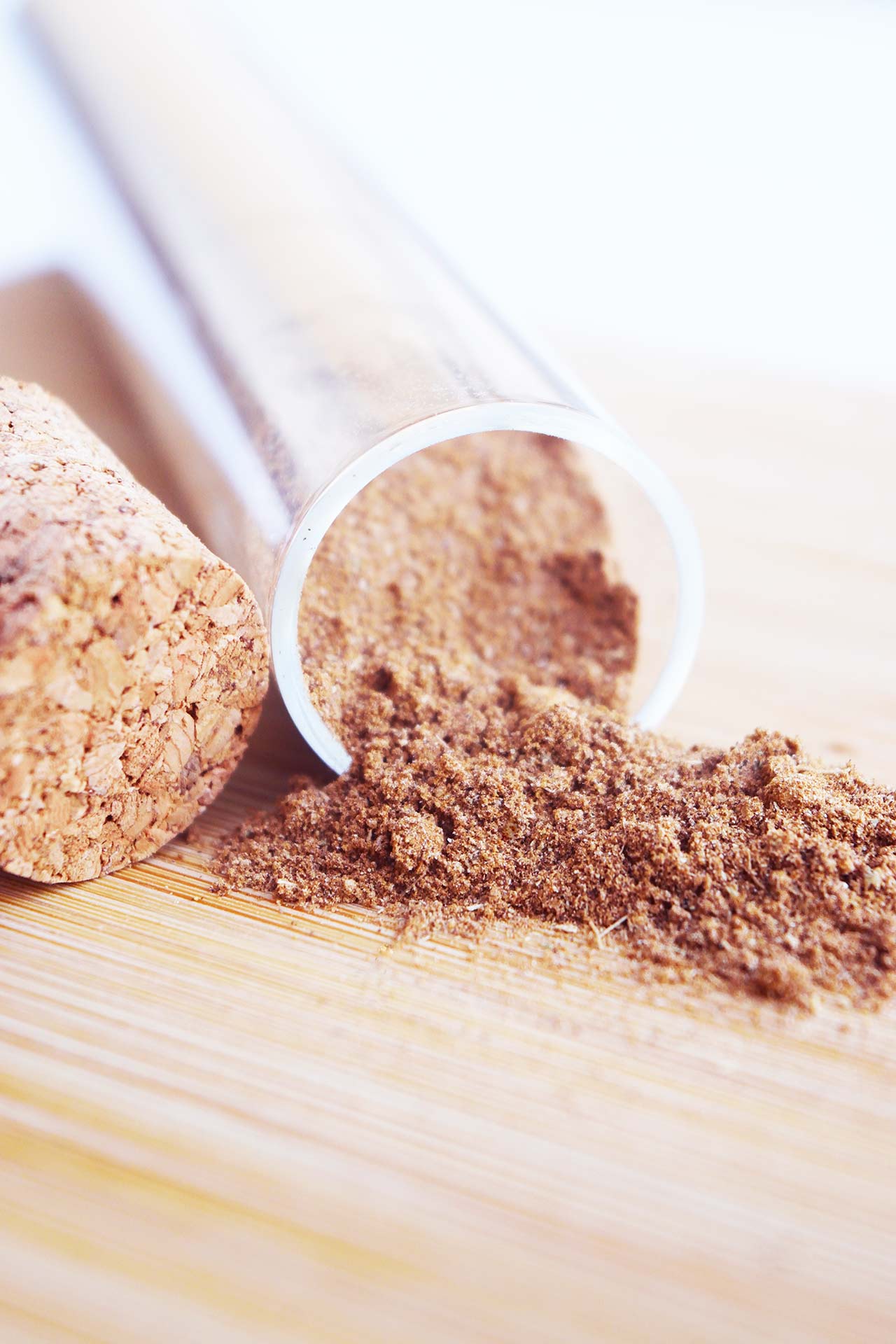 Closeup of a tipped over spice jar on a wood surface with chai spice mix falling out.