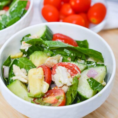 Front view of two bowls filled with Chicken And Collard Greens. A bowl of grape tomatoes sits in the background.