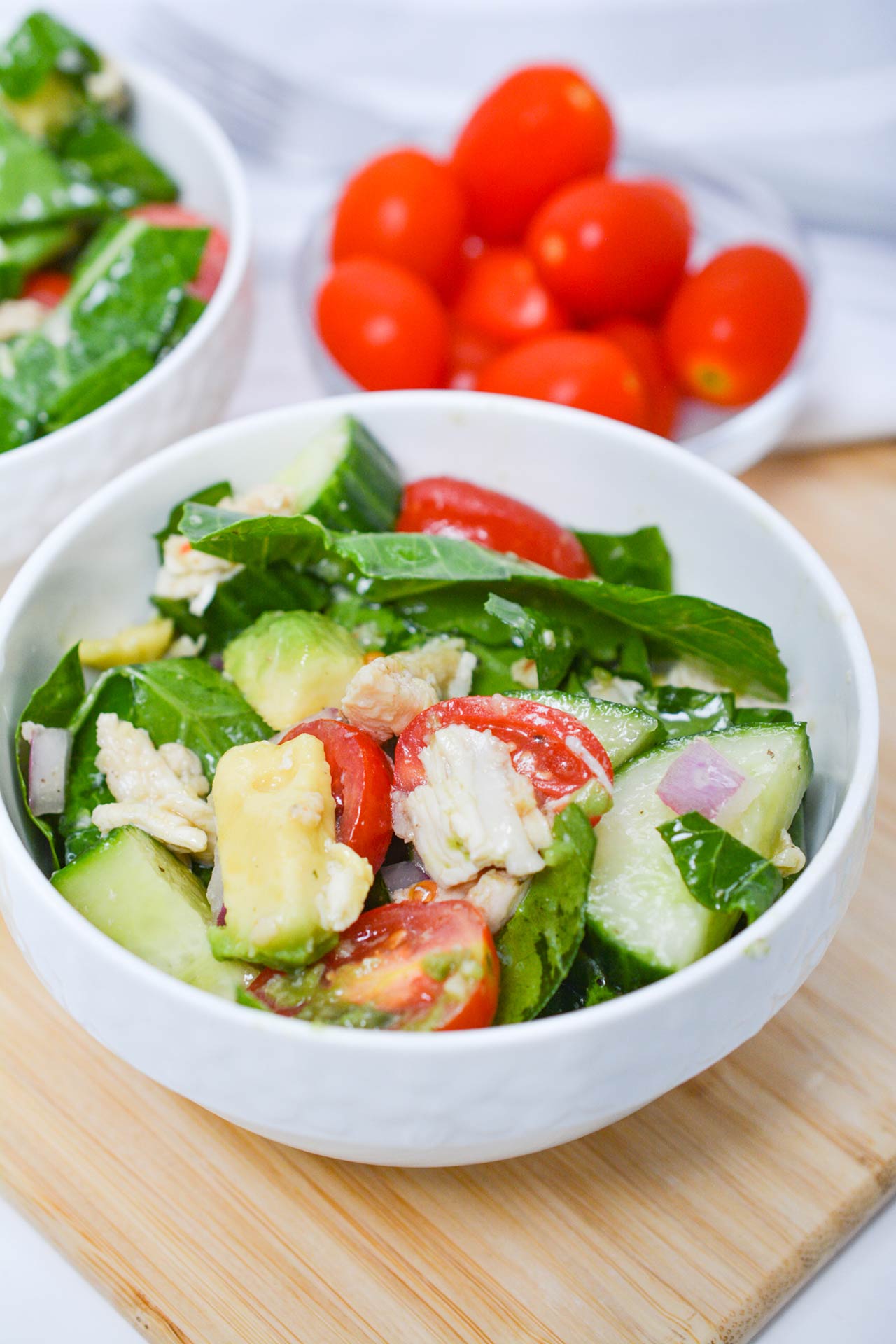 Front view of two bowls filled with Chicken And Collard Greens. A bowl of grape tomatoes sits in the background.